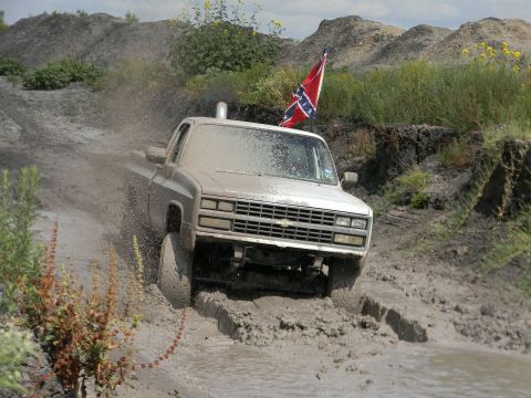 1989 Ford Bronco - This pickup truck is kicking up mud while navigating a rough, off-road terrain.