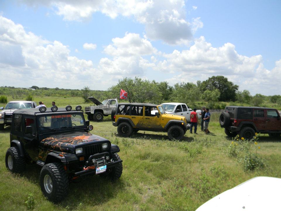 Several modified Jeep Wranglers and trucks parked in a grassy field under a cloudy sky