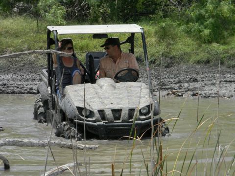 1989 Ford Bronco - Two people navigate a muddy off-road trail in a utility vehicle.