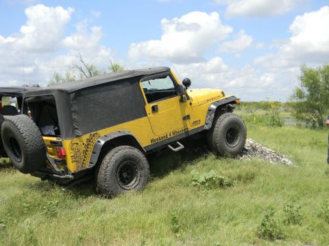 1989 Ford Bronco - A yellow Jeep Wrangler Rubicon navigates a grassy incline, with another Jeep visible in the background.