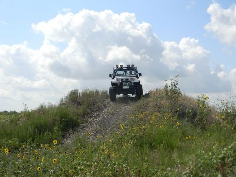 1989 Ford Bronco - A white Jeep Wrangler navigates an off-road trail under a cloudy sky.