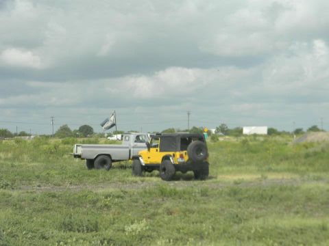 1989 Ford Bronco - Two off-road vehicles, a yellow Jeep and a silver pickup truck, are parked in a grassy field on a cloudy day.