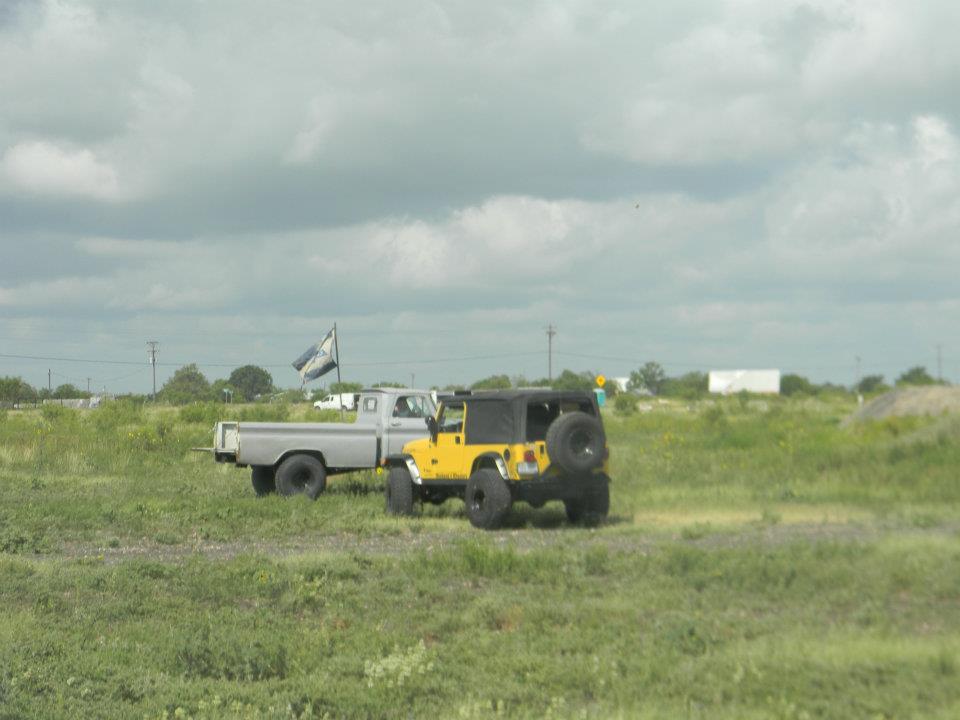 Yellow Jeep Wrangler and silver pickup truck in a field under a cloudy sky