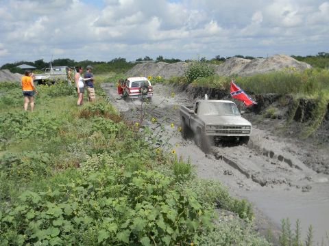 1989 Ford Bronco - Several off-road vehicles navigate a muddy track under a cloudy sky.