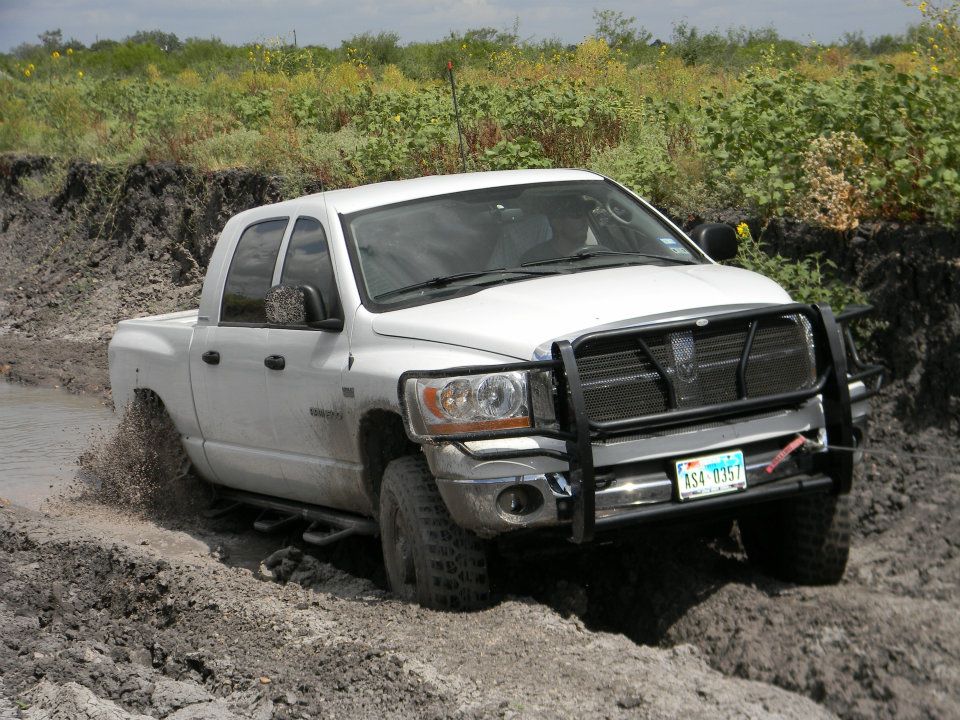 White Dodge Ram pickup truck driving through mud and water, front bull bar attached