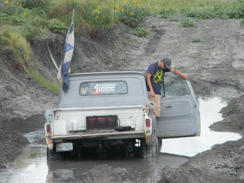 1989 Ford Bronco - A person exits a gray pickup truck that appears stuck in a muddy, watery track.