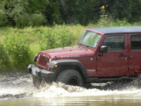 1989 Ford Bronco - Jeep Wrangler Rubicon splashes through water on a trail.