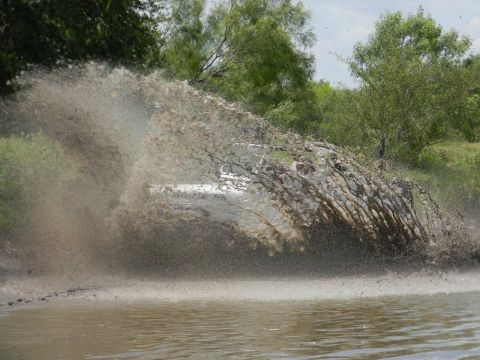 1989 Ford Bronco - A white SUV creates a massive splash as it drives through a muddy area.