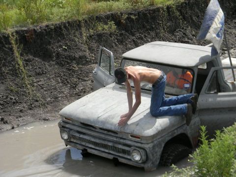 1989 Ford Bronco - A man is on the hood of a mud-covered pickup truck that is stuck in a ditch.