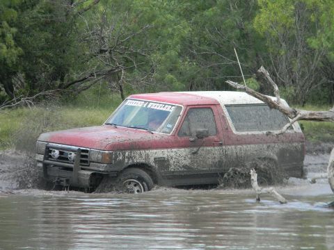 1989 Ford Bronco - This red and white Ford Bronco is deep in the mud, with its front bull bar partially submerged.
