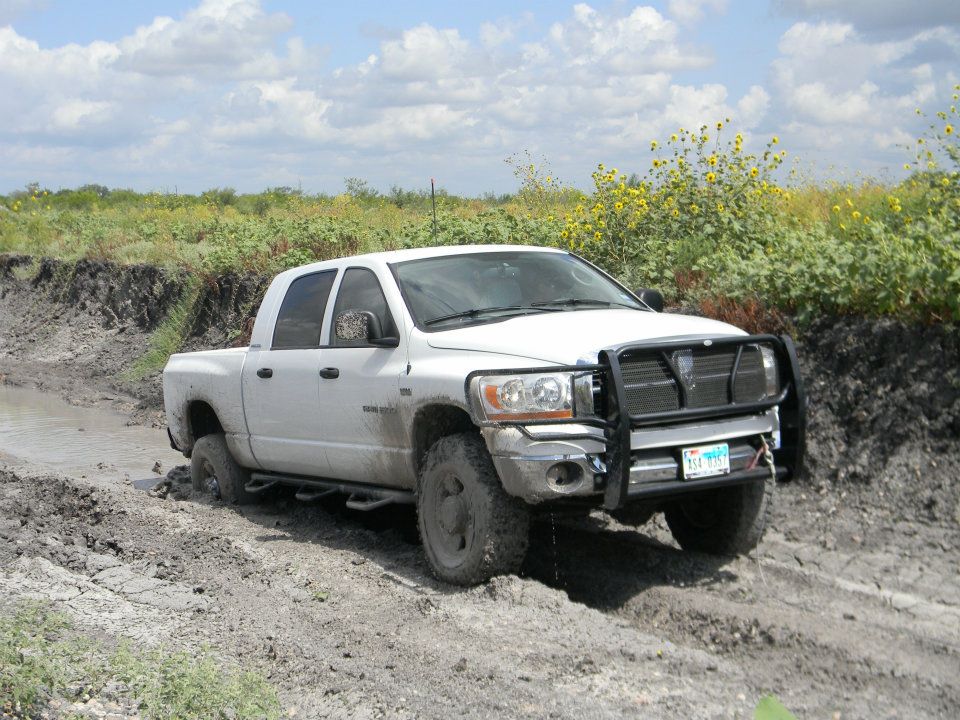 White Dodge Ram pickup truck with a bull bar stuck in a muddy ditch off-road