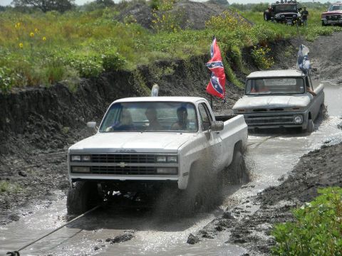 1989 Ford Bronco - Two pickup trucks navigate a muddy off-road course, one pulling the other with a tow rope.