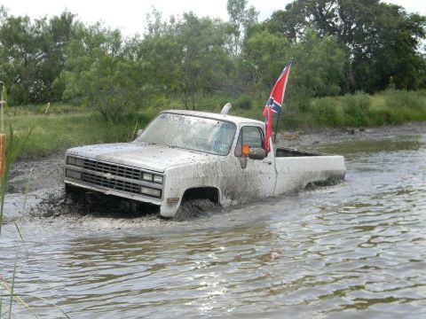 1989 Ford Bronco - White Chevrolet C/K pickup truck stuck in mud with a Confederate flag flying from the antenna.