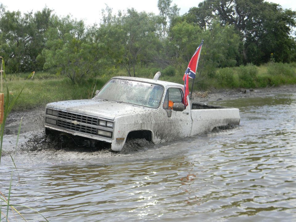 White Chevrolet C/K pickup truck stuck in mud, Confederate flag on antenna
