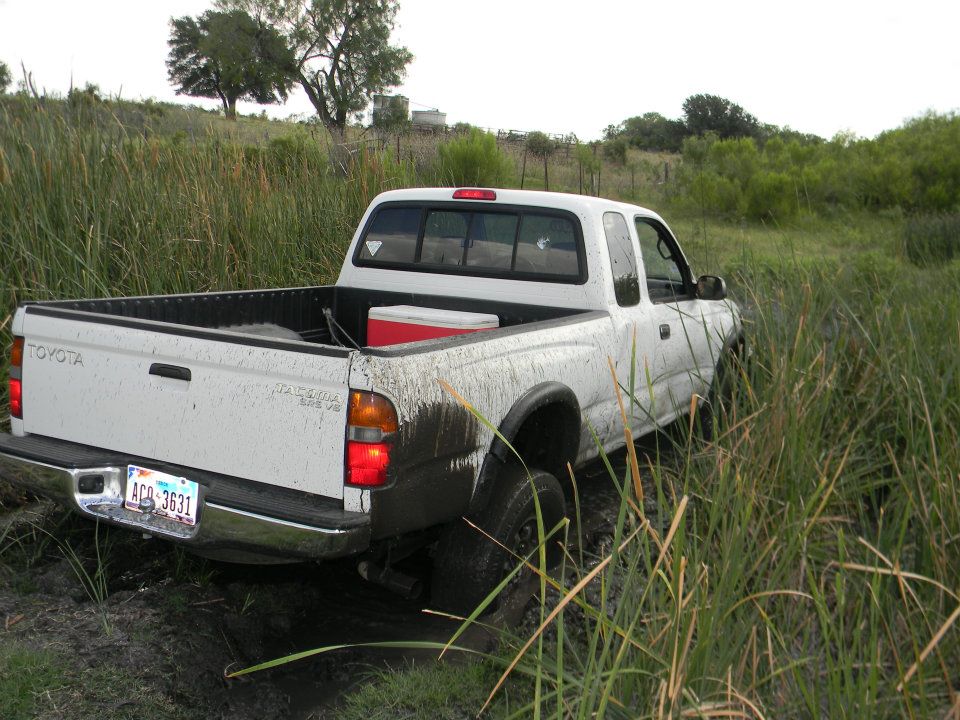 White Toyota pickup truck stuck in mud and tall grass. Cooler in bed
