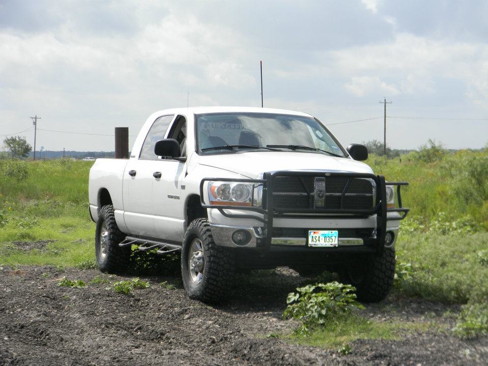 White Dodge Ram pickup truck with aftermarket brush guard and off-road tires parked on dirt