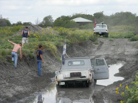 1989 Ford Bronco - Two pickup trucks navigate a muddy terrain with onlookers present.