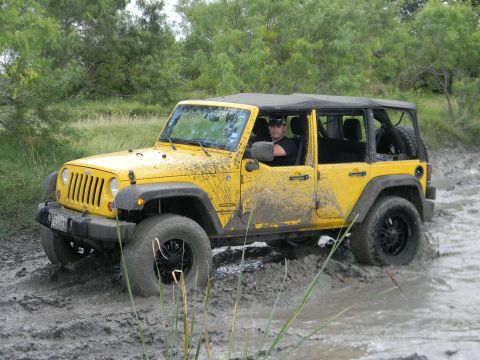 1989 Ford Bronco - A yellow Jeep Wrangler navigates a muddy trail, with its tires deep in the mire.
