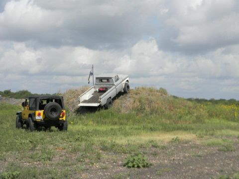 1989 Ford Bronco - Two off-road vehicles are parked on a grassy hill under a cloudy sky.