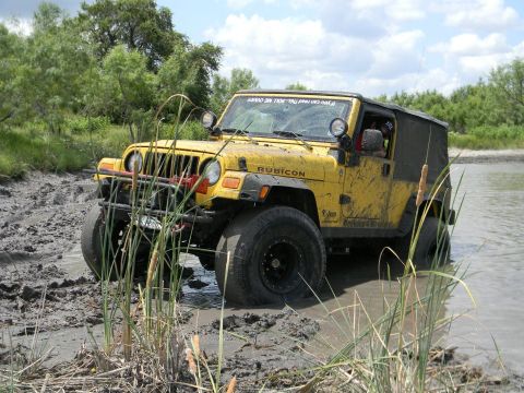 1989 Ford Bronco - This yellow Jeep Wrangler Rubicon is navigating through a muddy, watery terrain.