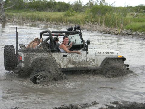 1989 Ford Bronco - A white Jeep Wrangler, adorned with a Harley Davidson decal, navigates through a muddy waterway, with passengers enjoying the off-road adve…