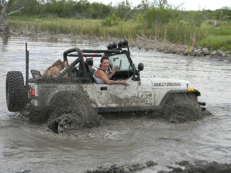 White Jeep Wrangler with Harley Davidson decal driving through mud