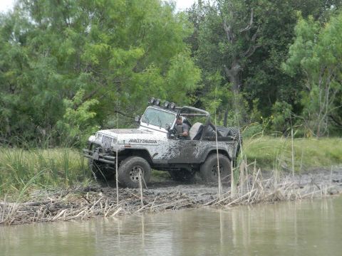 1989 Ford Bronco - This Jeep Wrangler navigates a muddy, watery terrain, its "Harley-Davidson" decal visible through the mud splatters.