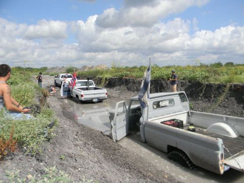 1989 Ford Bronco - Trucks are bogged down in a muddy trench under a cloudy sky.
