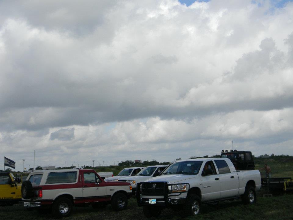 Red and white Ford Bronco with spare tire on rear, parked next to white Dodge Ram pickup truck