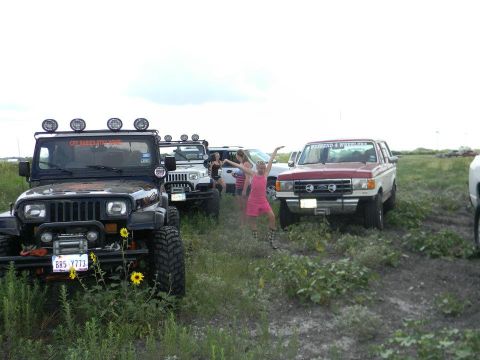 1989 Ford Bronco - A group of off-road vehicles are gathered in a field with people enjoying the outdoors.