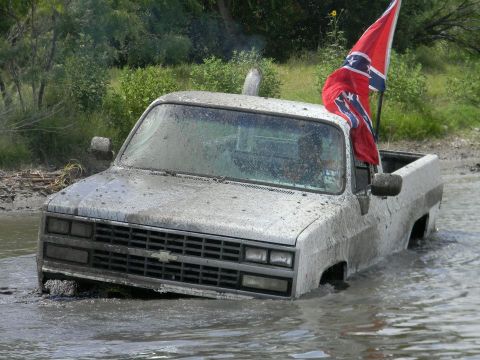 1989 Ford Bronco - Pickup truck stuck in mud and water, flying a Confederate flag.