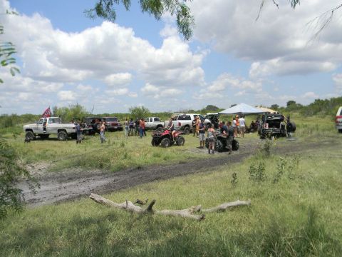 1989 Ford Bronco - A gathering of off-road vehicles and people in a muddy field on a partly cloudy day.