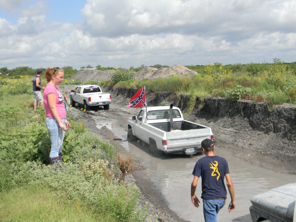 White pickup truck with Confederate flag driving through mud, rear view