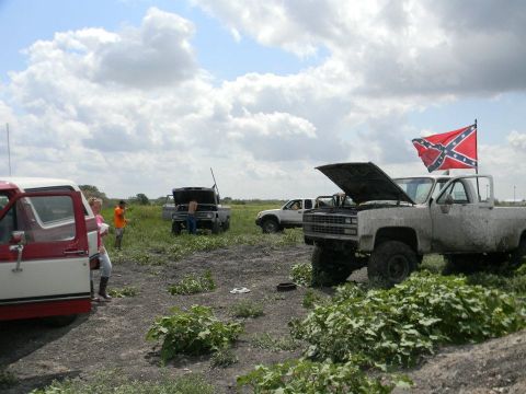 1989 Ford Bronco - Multiple trucks are gathered in a field, some with their hoods open, under a cloudy sky.
