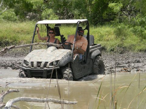 1989 Ford Bronco - Two people navigate a muddy off-road trail in a utility vehicle.