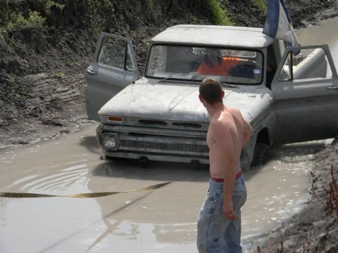 1989 Ford Bronco - This old pickup truck is stuck in a muddy ditch with a person inside and another person standing nearby.