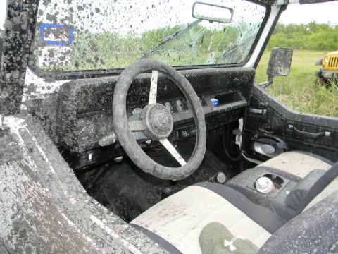1989 Ford Bronco - The interior of a vehicle is covered in mud after off-roading, with another vehicle in the background.