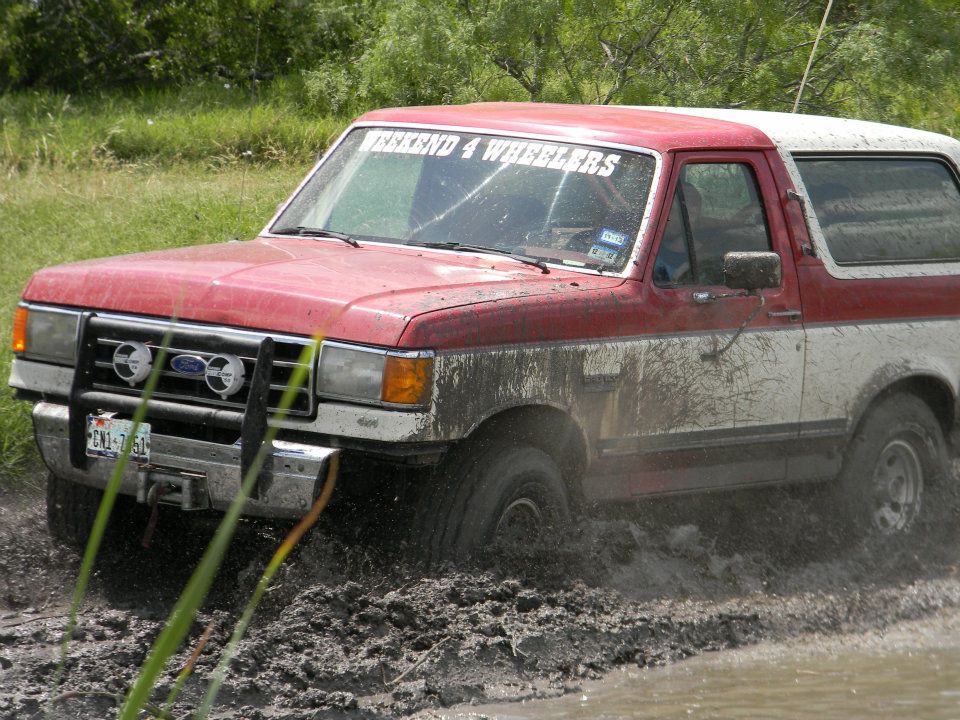 1989 Ford Bronco driving through mud, red and white paint, "WEEKEND 4 WHEELERS" sticker on windshield