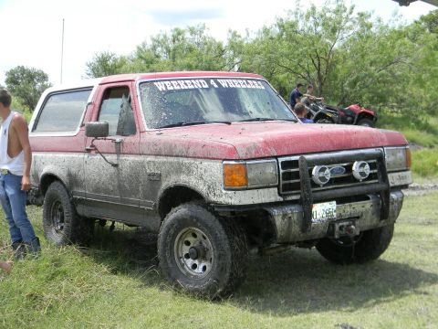 1989 Ford Bronco - This muddy Ford Bronco appears to be from the late 1980s, not a 1989 model, with a "Weekend 4 Wheelers" banner on the windshield.