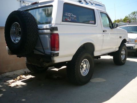 1988 Ford Bronco - This white Ford Bronco is parked outdoors next to another vehicle, with a spare tire on the rear.