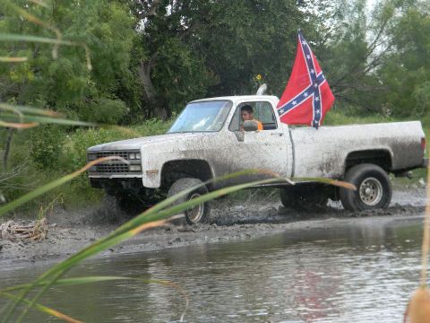 1989 Ford Bronco - A white pickup truck is shown navigating a muddy, watery terrain with a confederate flag displayed.