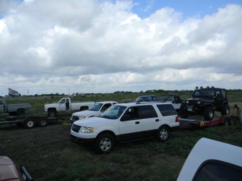1989 Ford Bronco - A collection of trucks and SUVs are parked in a grassy field on a cloudy day.