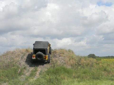 1989 Ford Bronco - A yellow Jeep Wrangler navigates an off-road trail on a cloudy day.
