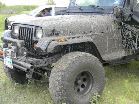 1989 Ford Bronco - A heavily mud-caked Jeep Wrangler is parked next to another vehicle in a grassy area.