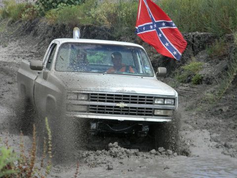 1989 Ford Bronco - Chevrolet pickup truck navigates a muddy terrain with a Confederate flag visible.