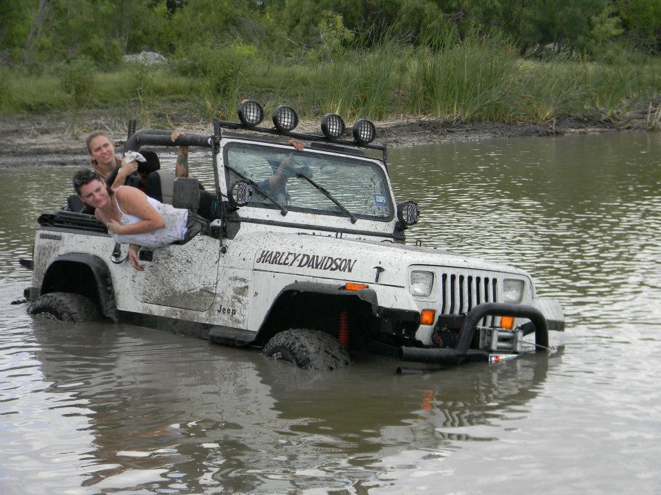White Jeep Wrangler with Harley Davidson decal stuck in water, two women inside