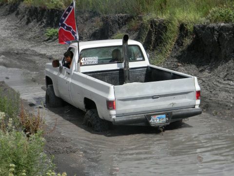 1989 Ford Bronco - Pickup truck navigates a muddy off-road course, flying a Confederate flag and sporting a large exhaust stack.