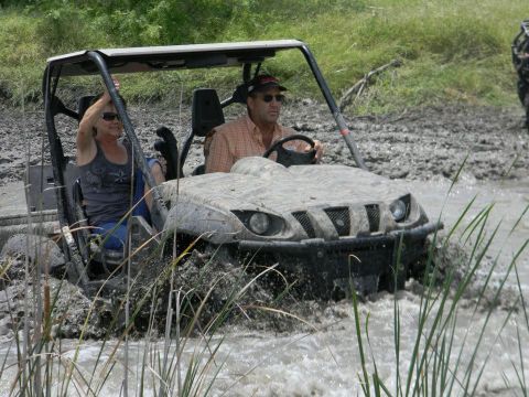 1989 Ford Bronco - A couple navigates a muddy waterway in an off-road vehicle, with another vehicle visible in the background.