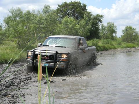 1989 Ford Bronco - A GMC pickup truck navigates through a muddy, watery terrain, kicking up spray.