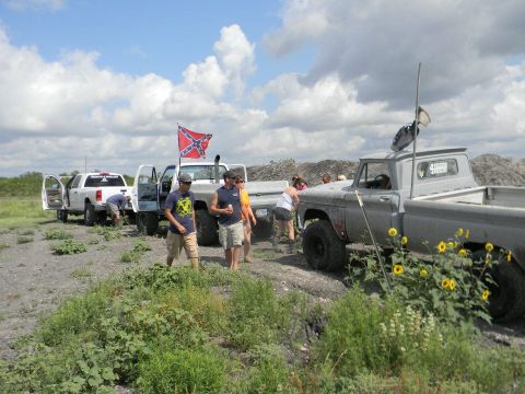 1989 Ford Bronco - Several trucks and people are gathered in a dusty, outdoor area under a cloudy sky.